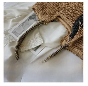 Detail of woven straw handbag with two-tone braided handle and black tassel ornament