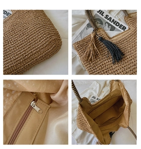 Detail view of woven straw tote bag featuring tassel charms and internal zipper pocket