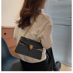 Detail of a black faux-leather chain bag featuring a golden lion head and crocodile texture