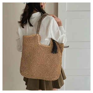 Straw tote bag with black tassel and striped handles worn by a model in a casual outfit