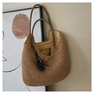 Detail of woven straw tote bag with long tassels and thin braided shoulder strap