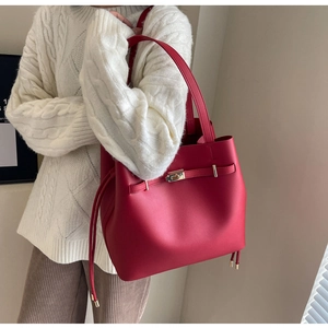 Red leather tote bag with gold buckle and tassel drawstring shown on model side view