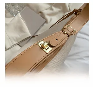 Detailaufnahme des goldenen Metalldrehverschlusses an einer beigen Canvas-Schultertasche