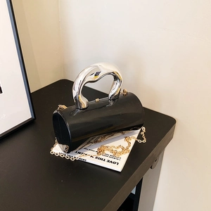 Detail der minimalistischen Zylindertasche mit skulpturalem Silbergriff und goldener Kette