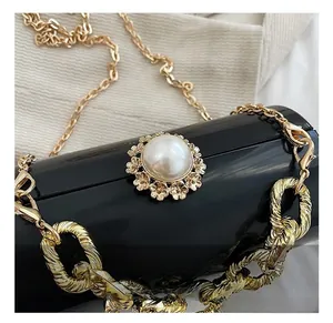 Detail einer schwarzen glänzenden Handtasche mit Perlenverschluss und goldenen Ketten