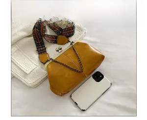 Detail view of mustard yellow vintage kiss-lock bag with wide ethnic strap and phone for scale