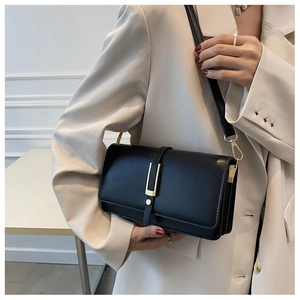 Borsa a tracolla minimalista in pelle nera con fibbia dorata a U su un blazer beige