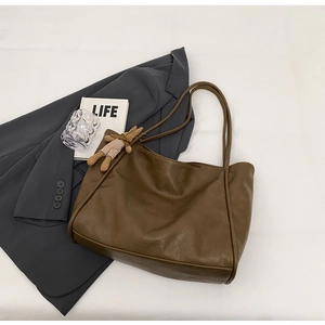 Detail einer dunkelbraunen Leder-Tote-Bag mit Kaninchen-Anhänger auf grauem Blazer