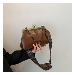Detail of vintage brown glossy leather bag with metal frame and wide patterned strap
