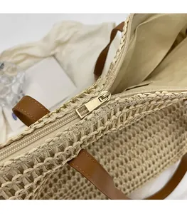 Close-up of smooth gold-tone zipper hardware on a beige woven tote bag with leather straps
