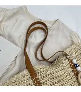 Detail of woven straw shoulder bag with brown leather strap and blue beaded ornament