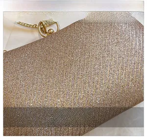 Détail de pochette dorée champagne scintillante avec texture verticale et poignée en strass