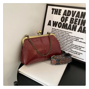 Detail of wine red clutch bag with bohemian shoulder strap and retro clasp on books