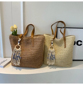 Detail of woven straw tote bags featuring evil eye tassels and brown leather handles
