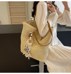 Macro detail of straw woven tote bag featuring evil eye charm and leather strap