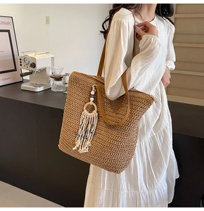 Detail of hand-woven straw tote bag with brown leather strap and bohemian tassel charm