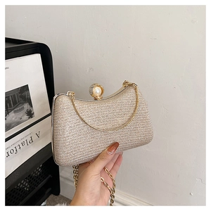Elegant champagne glitter evening bag with pearl clasp and gold chain held by hand