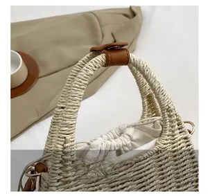 Detail of hand-woven beige straw bag featuring leather buckle and canvas drawstring liner