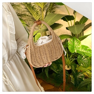 Detail of woven straw handbag featuring a drawstring lining and brown leather strap