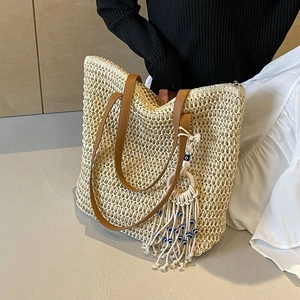 Large beige woven straw tote bag with brown faux leather straps and evil eye tassel charm