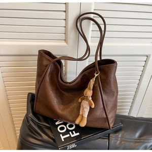 Braune Shopper-Tasche aus Kunstleder mit Hasenanhänger vor einem weißen Fensterladen-Hintergrund