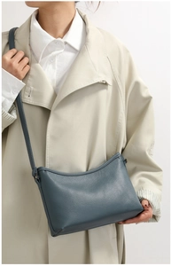 Detail of greyish-blue crossbody bag with lychee texture worn over a khaki trench coat