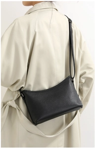 Detailed view of black pebble leather hobo bag worn with a classic trench coat