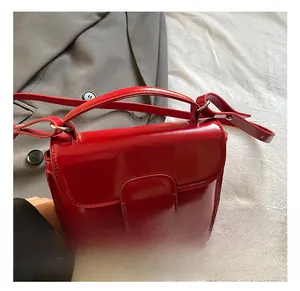 Detail of red glossy leather handbag with refined buckle closure and adjustable strap
