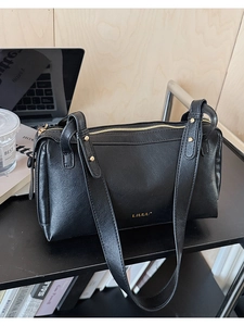 Detail shot of black leather vintage pillow bag with gold zipper on an office desk