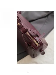 Detailed close-up of smooth gold zipper and lychee pattern leather on dark red bag