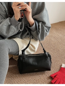Detail of classic black leather pillow bag featuring gold metal zipper and brand logo
