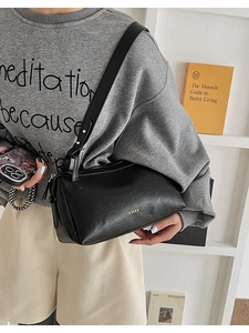 Close-up of black leather pillow bag featuring golden logo and textured finish