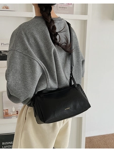 Detail of black pebbled leather pillow bag with gold logo and adjustable shoulder strap