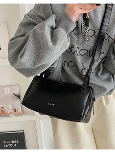 Detail of minimalist black matte leather pillow bag with gold logo and adjustable strap