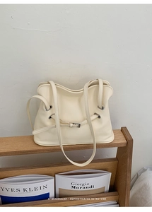 Detalle del bolso tote crema minimalista con ojales metálicos en soporte de madera