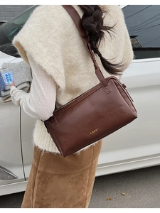 Detail of a dark brown vintage pillow bag with golden logo on a shoulder strap