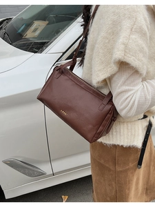 Close-up of a brown leather pillow bag with gold logo on a textured knit outfit