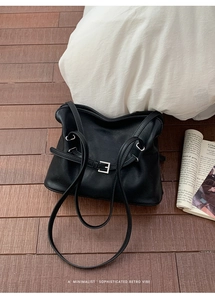 Detalle de bolso tote plisado negro minimalista con asa fina sobre madera