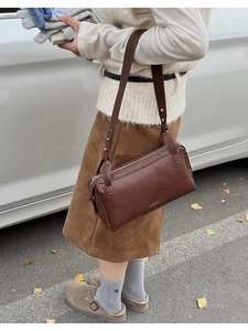 Detail of dark brown vintage pillow bag with gold logo on an autumn street setting