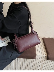 Detail of burgundy leather shoulder bag with gold metal logo and zipper closure