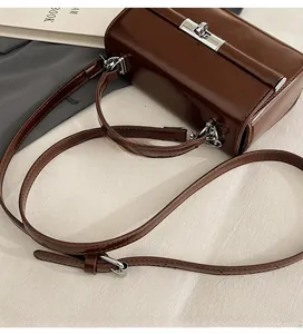 Détail d'un sac à main en cuir marron brillant avec fermoir argenté et bandoulière
