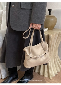 Detalle de bolso de hombro beige plisado con hebilla y textura de cuero suave
