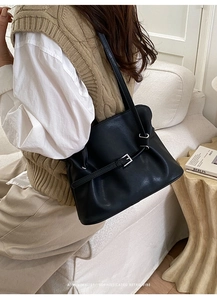 Detalle de bolso tote negro de cuero sintético con hebilla en un sofá minimalista