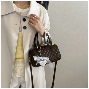 Close-up of quilted dark brown Boston bag with pearl heart charm and lace detail