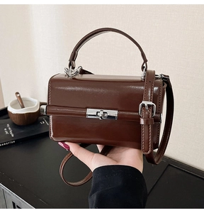 Détail d'un sac à main marron brillant avec fermoir rotatif argenté et forme boîte structurée