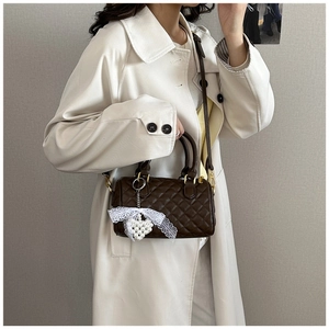 Detail of dark brown quilted Boston bag with pearl heart charm on trench coat outfit