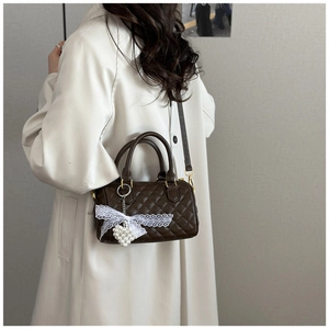 Detail of dark brown quilted Boston bag featuring lace bow and pearl heart charm