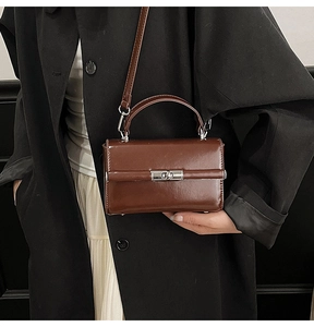 Détail du sac à main en cuir marron foncé avec fermoir argenté sur un trench noir