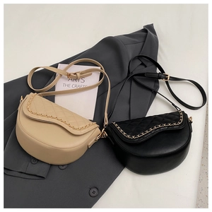 Quilted saddle bags in beige and black with gold chain trim on grey blazer background