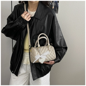 Detail of beige quilted Boston bag featuring pearl heart charm and lace bow decor